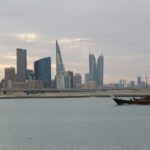 The Bahraini capitals skyline just after sunrise. A boat can be seen sailing in front.