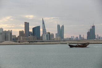 The Bahraini capitals skyline just after sunrise. A boat can be seen sailing in front.