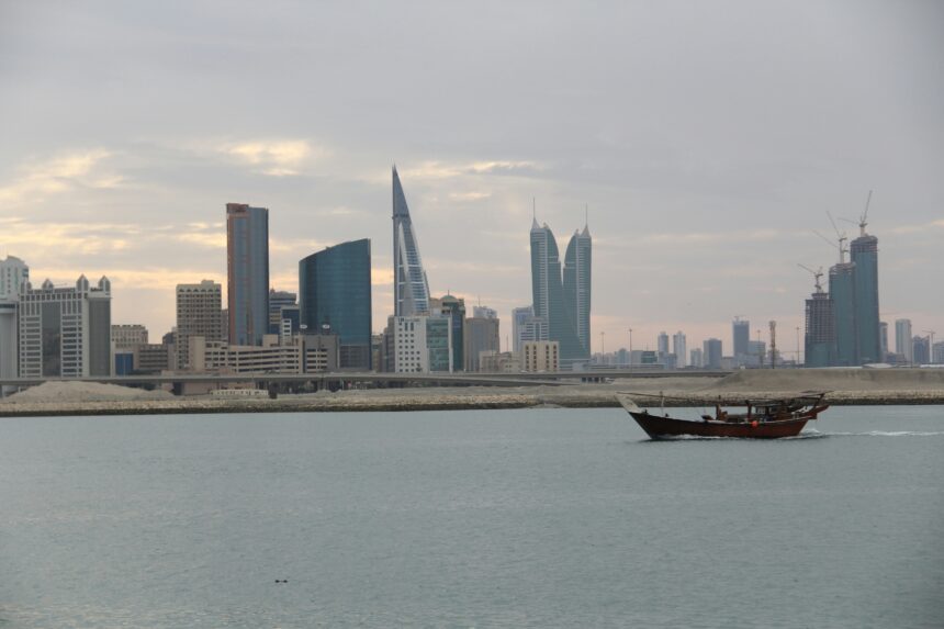The Bahraini capitals skyline just after sunrise. A boat can be seen sailing in front.