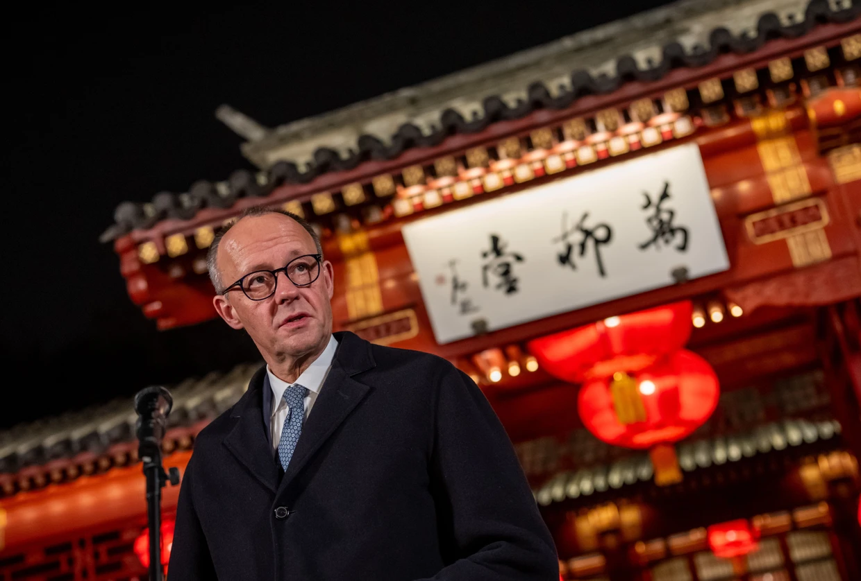 German Chancellor Friedrich Merz standing in front of a building with Chinese characters written on it.