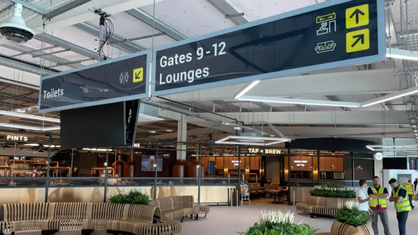 Image of Leeds Bradford Airport, signs showing gates and lounges above a large space in the airport.
