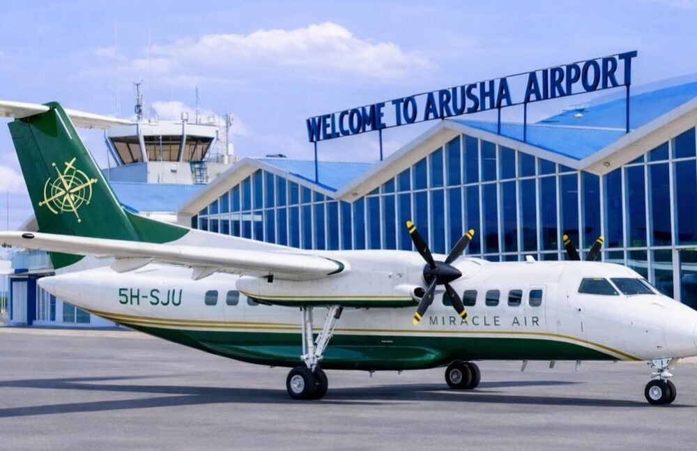 Miracle Air Dash 8 5H-SJU in front of a building that reads "Welcome to Arusha Airport".
