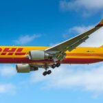 DHL Boeing aircraft flying in the sky. Blue sky and clouds in the background. Yellow livery.