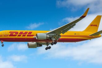 DHL Boeing aircraft flying in the sky. Blue sky and clouds in the background. Yellow livery.
