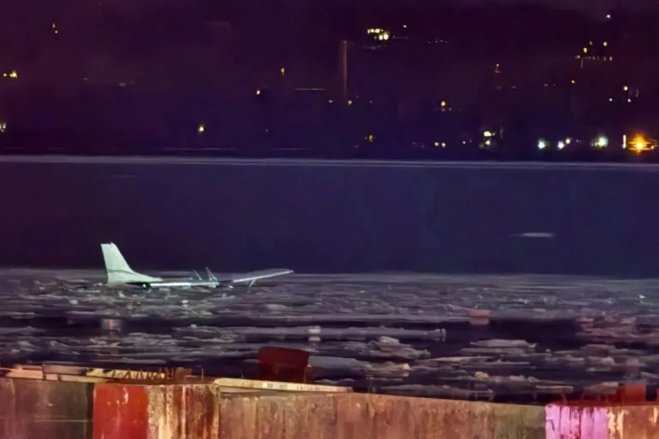 A wider view showing the aircraft floating on the water with city buildings in the background.