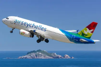 An Air Seychelles aircraft taking flight between blue, clear skies and blue seas, with an island in the centre of the sea below.