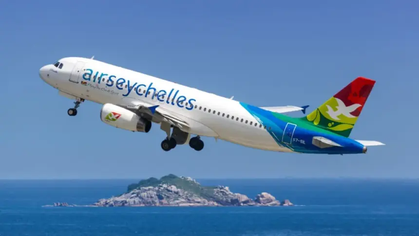 An Air Seychelles aircraft taking flight between blue, clear skies and blue seas, with an island in the centre of the sea below.