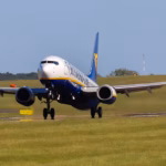 A Ryan Air aircraft taking flight with runway and green space beneath it as the aircraft leaves the ground.