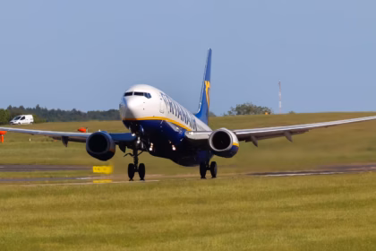 A Ryan Air aircraft taking flight with runway and green space beneath it as the aircraft leaves the ground.