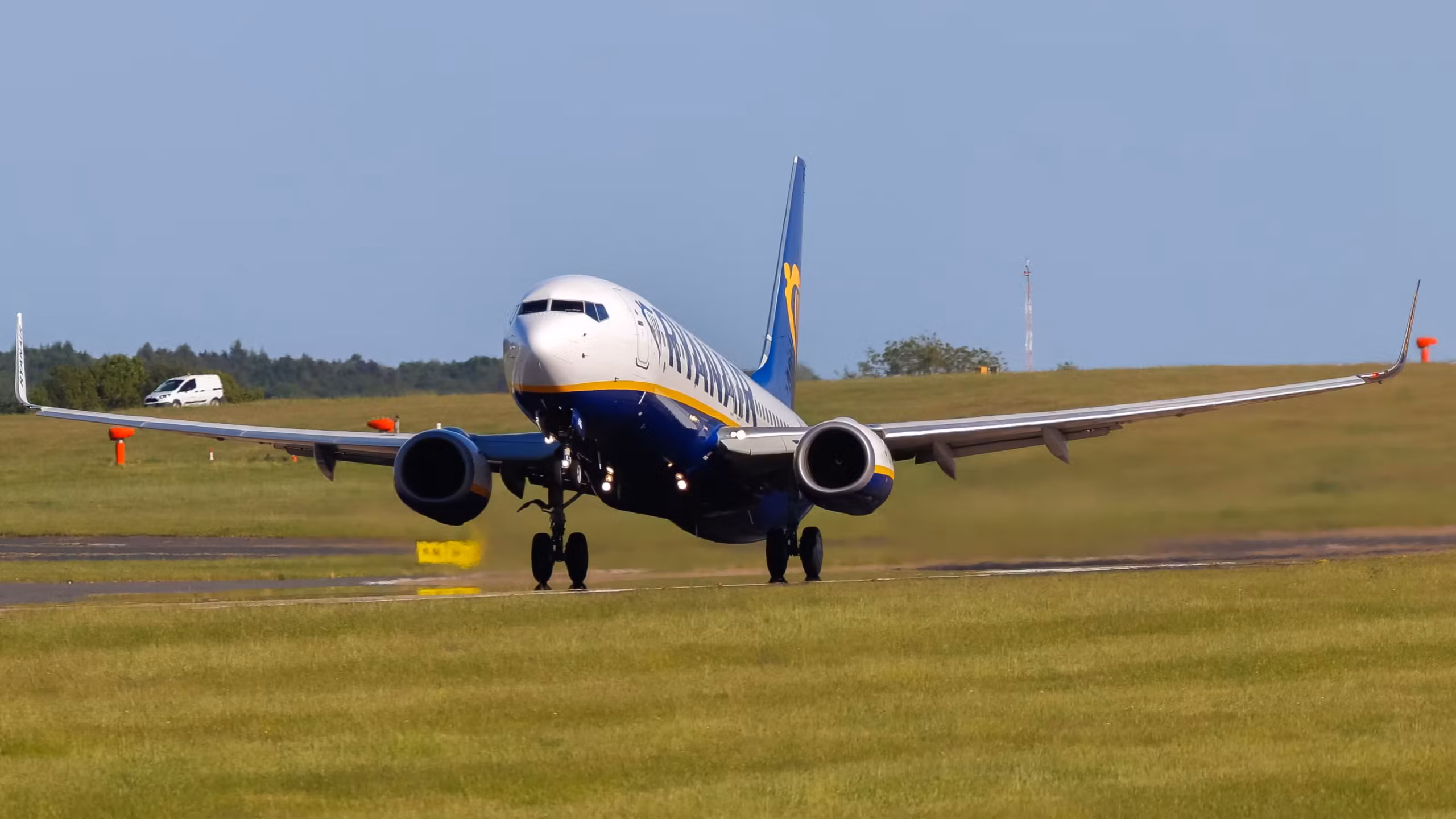 A Ryan Air aircraft taking flight with runway and green space beneath it as the aircraft leaves the ground.