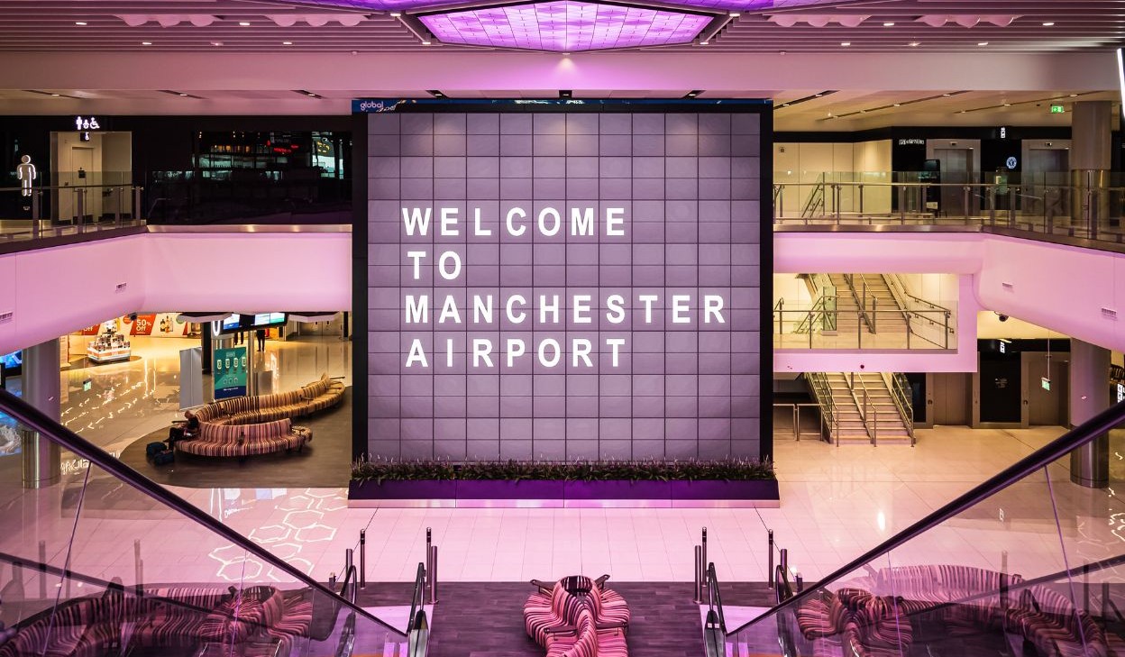 A large sign reading 'Welcome to Manchester Airport' inside an entrance lobby