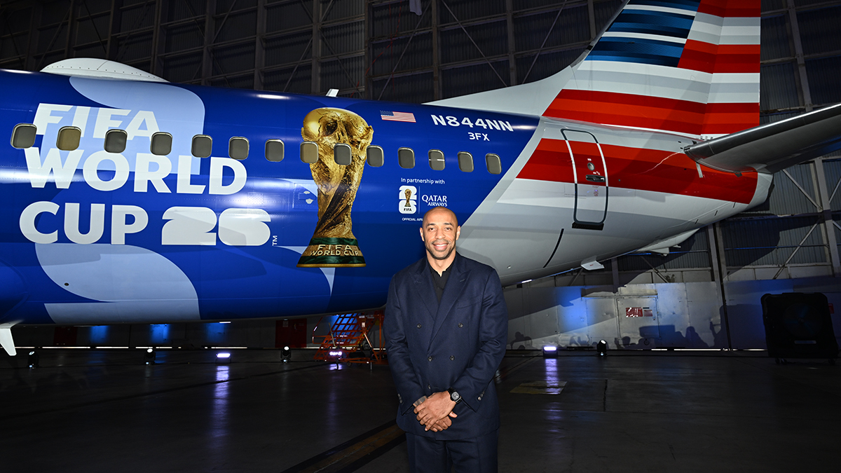 Image shows French Footballer Thierry Henry in front of American Airlines' FIFA World Cup 26-themed aircraft livery at night time.