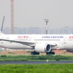 A white China Eastern Airlines wide-body airplane taxiing on a runway, viewed from the side in hazy daylight.