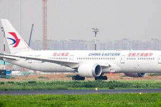 A white China Eastern Airlines wide-body airplane taxiing on a runway, viewed from the side in hazy daylight.