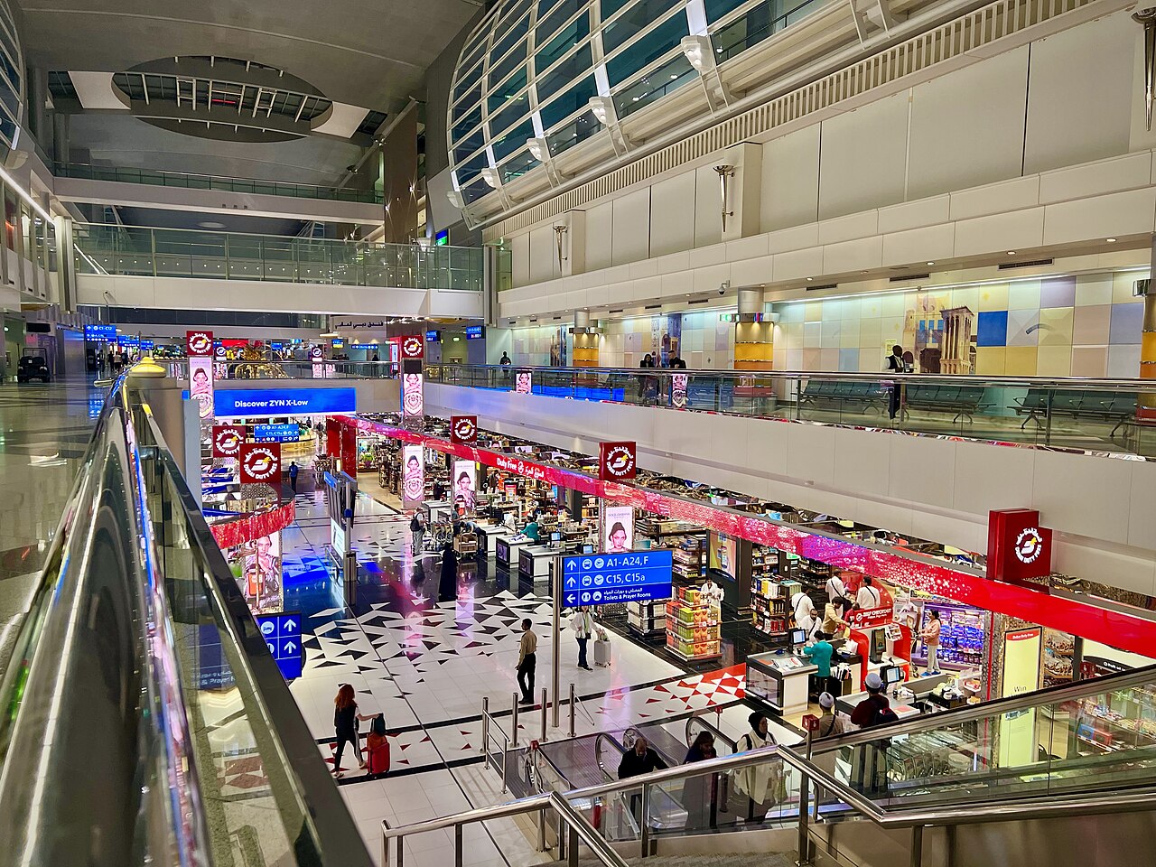 Dubai International Airport interior, neon lighting outside shops, people walking with suitcaes.