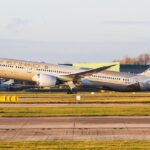 Etihad Airways B787 taking off at Manchester Airport in front of a grey sky, the sun shining on the aircraft.