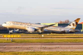 Etihad Airways B787 taking off at Manchester Airport in front of a grey sky, the sun shining on the aircraft.