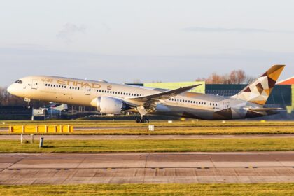 Etihad Airways B787 taking off at Manchester Airport in front of a grey sky, the sun shining on the aircraft.