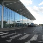 Glass-fronted terminal at Bristol Airport with buses parked outside and a roadway with pedestrian crossing.