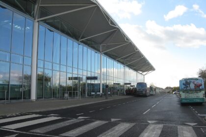 Glass-fronted terminal at Bristol Airport with buses parked outside and a roadway with pedestrian crossing.