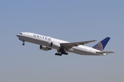 A United Airlines wide-body jet climbs into the sky after takeoff, angled upward with its landing gear still partially extended.