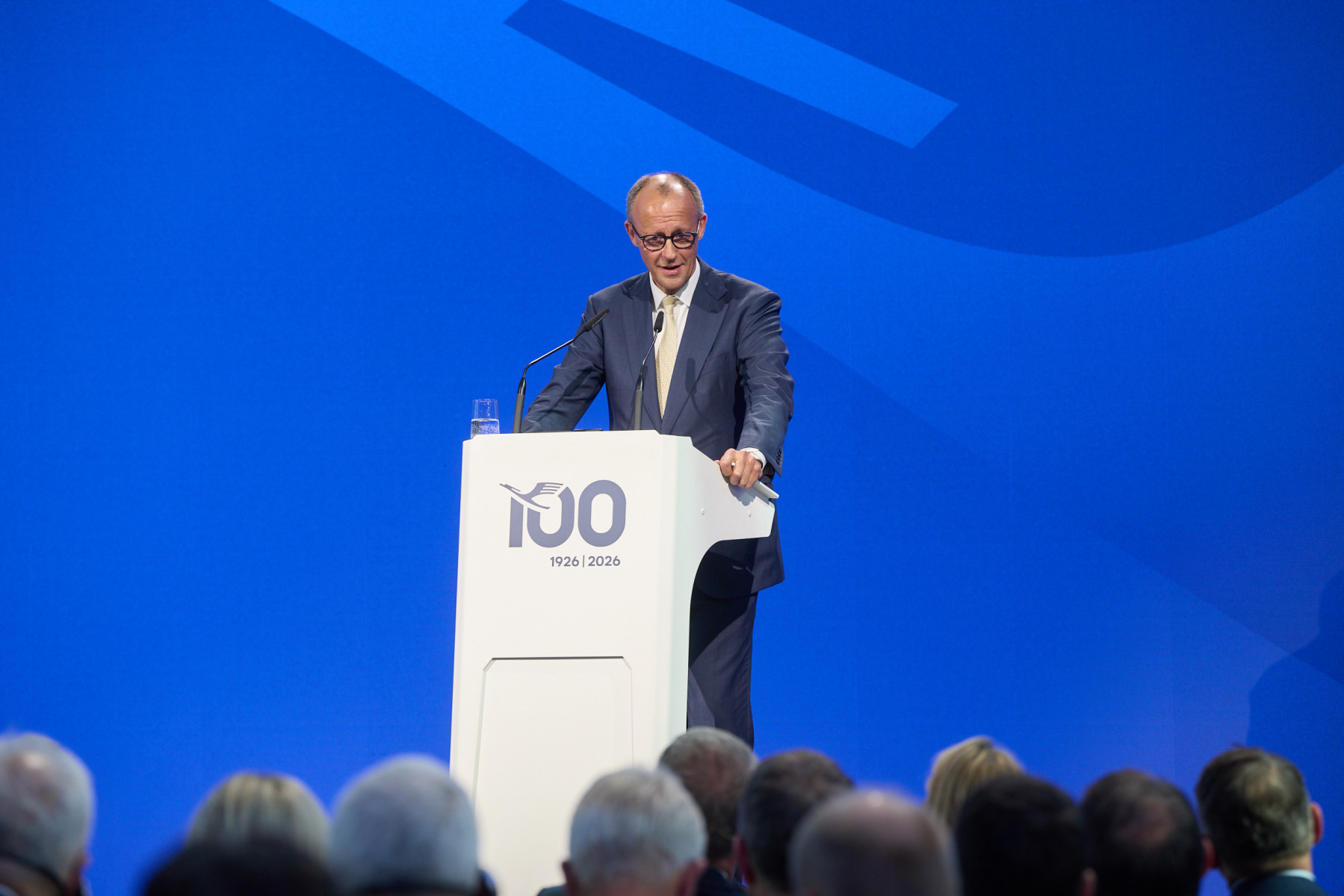 German Chancellor Friedrich Merz, standing at a white podium against a blue background