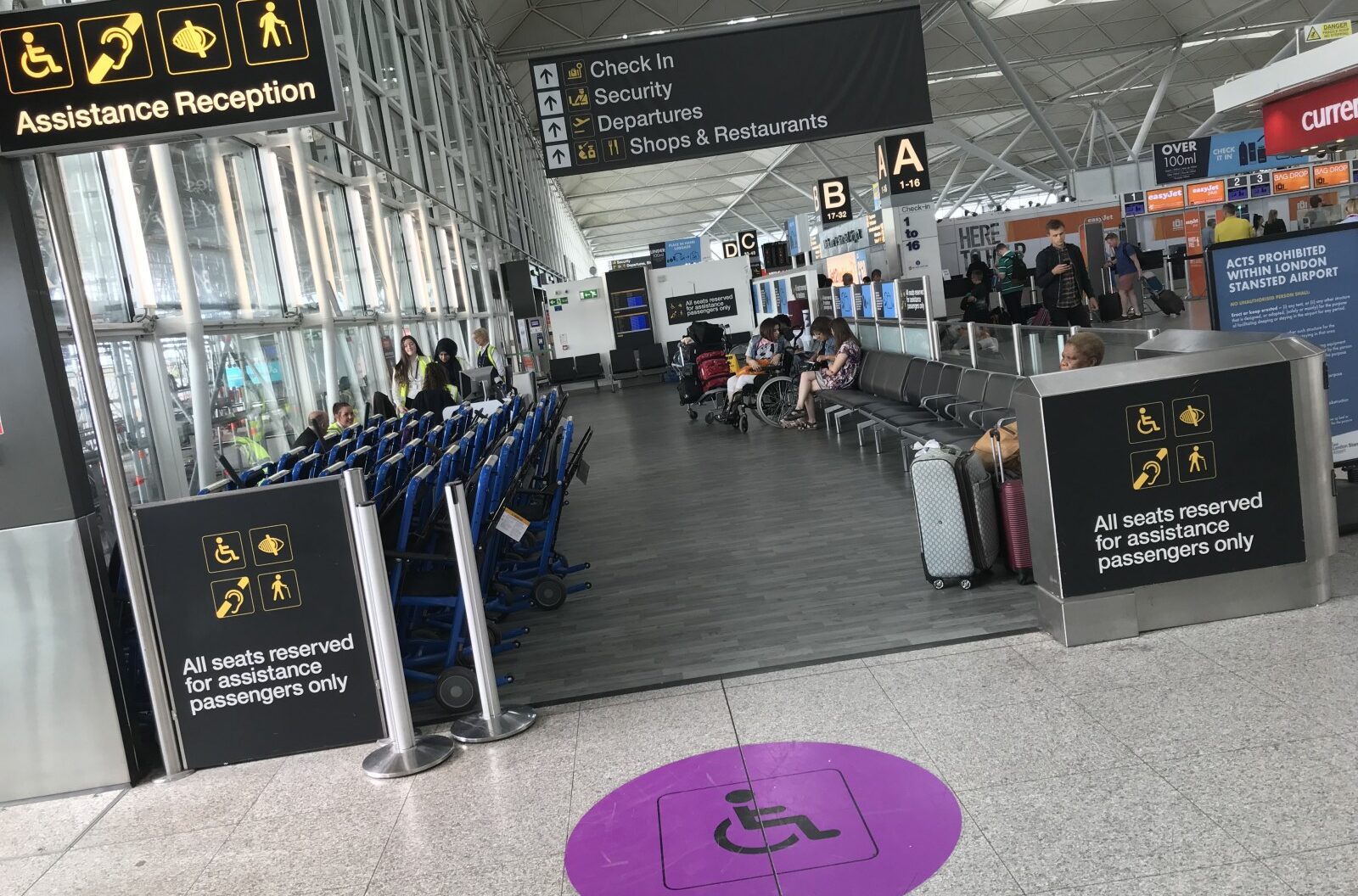 Image of Stansted Airport interior, with large black boards of information and purple disabled access stickers on the floor.
