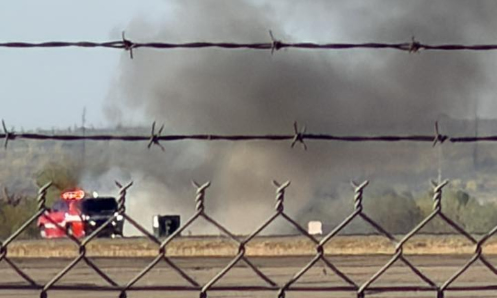 Metal fence in foreground, fire truck in the background next to large cloud of smoke.