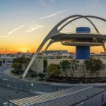 Sunrise over Los Angeles International Airport with aircraft silhouettes on the tarmac under an orange sky.