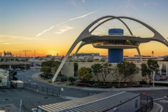 Sunrise over Los Angeles International Airport with aircraft silhouettes on the tarmac under an orange sky.