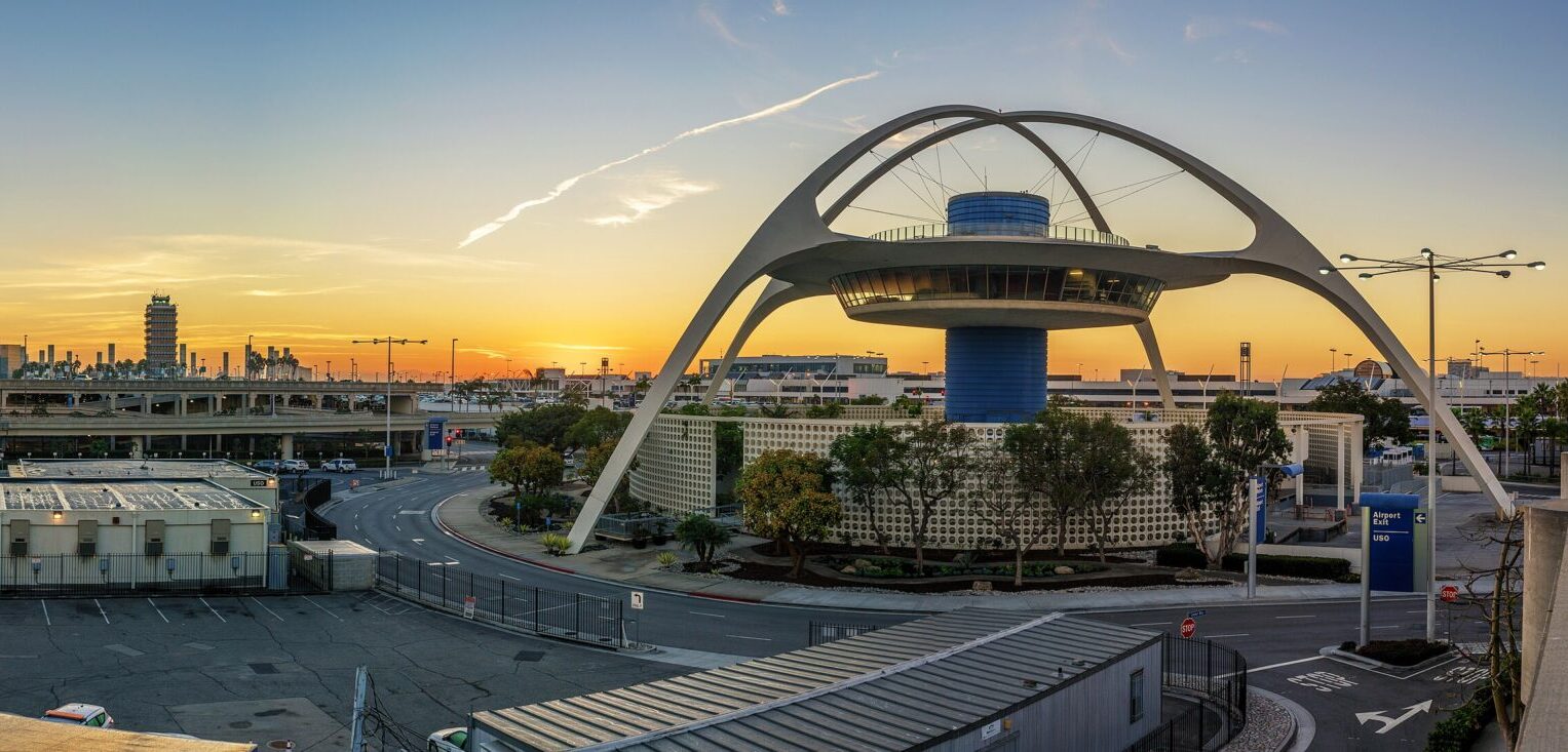 Sunrise over Los Angeles International Airport with aircraft silhouettes on the tarmac under an orange sky.