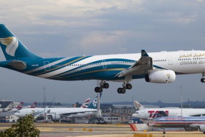 An Oman Air aircraft landing in Heathrow Airport. The aircraft is blue and white and is landing on a gravelly track among other aircrafts.