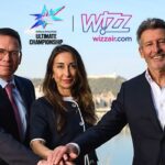 Two men, one woman with their hands in together in front of them, "Wizz Air" and "Ultimate Championship" written behind them.