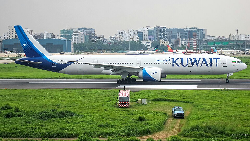 A wide-body jet on the runway with US-Bangla and Biman Bangladesh aircraft in the background, set against the urban backdrop of Bangladesh's capital. 