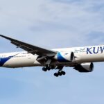 A Kuwait Airways Boeing 777-369(ER), registration 9K-AOJ, named "Al-Mesila." Flying against a blue sky.