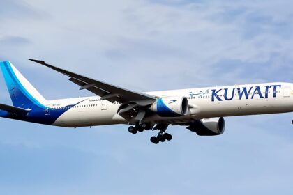 A Kuwait Airways Boeing 777-369(ER), registration 9K-AOJ, named "Al-Mesila." Flying against a blue sky.