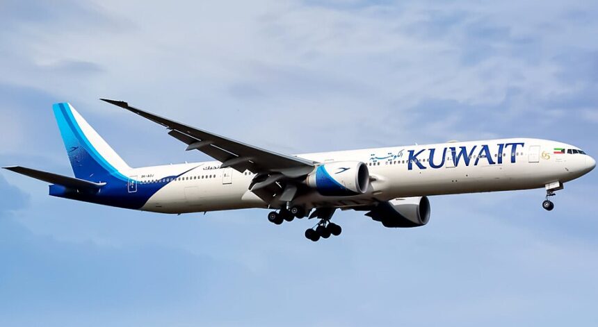 A Kuwait Airways Boeing 777-369(ER), registration 9K-AOJ, named "Al-Mesila." Flying against a blue sky.