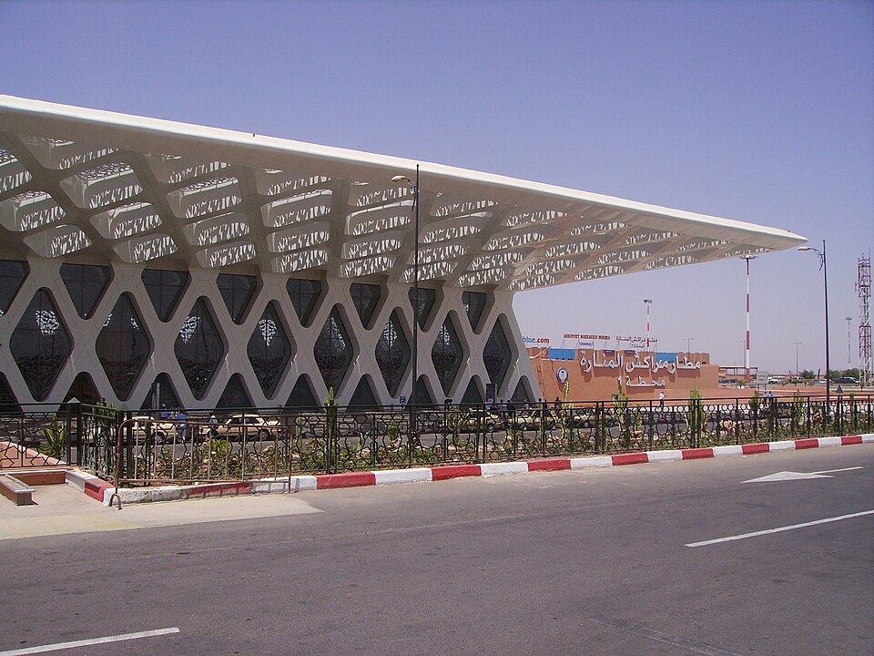 Marrakesh Menara Airport, there are railings in font of the building, blue sky in the background, and the road is shown.