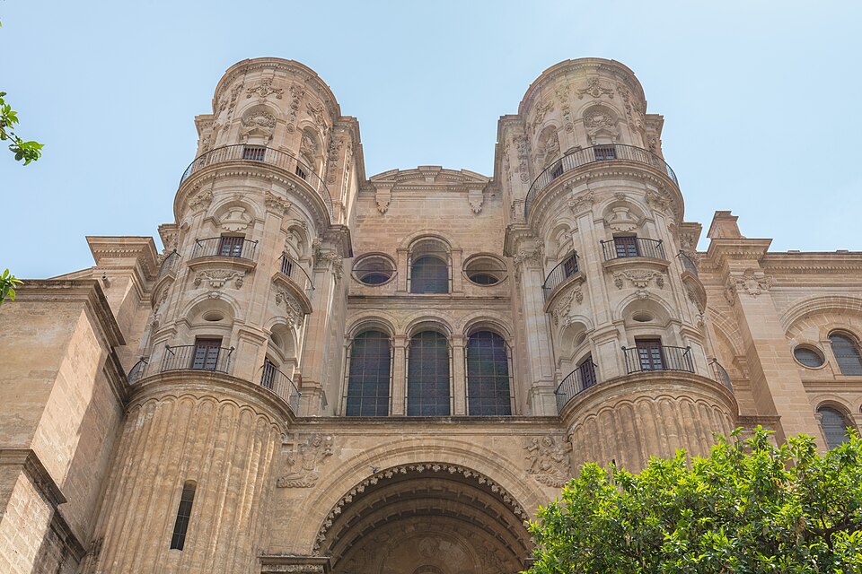 The Cathedral of the Incarnation in Málaga, low angle view, trees in the bottom right corner, blue sky above.