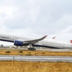 British Airway plane in the centre of the image taking off (facing towards the left). It has the British Airway flag logo on the tail. It is an overcast day in the background
