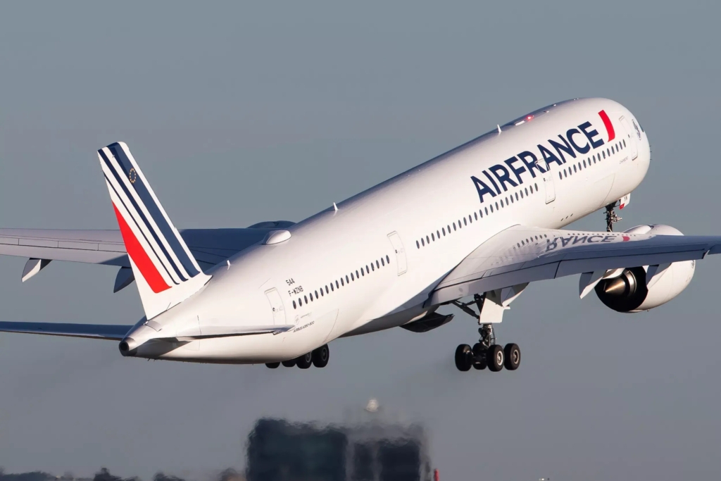 Air France white, blue and red plane taking flight, with buildings just below, amid grey-blue skies. 