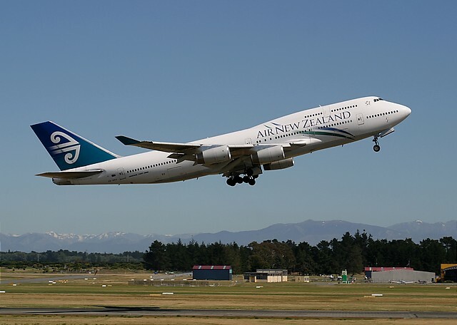 Air New Zealand Boeing 747-400 taking off with landing gear extended against a clear sky.