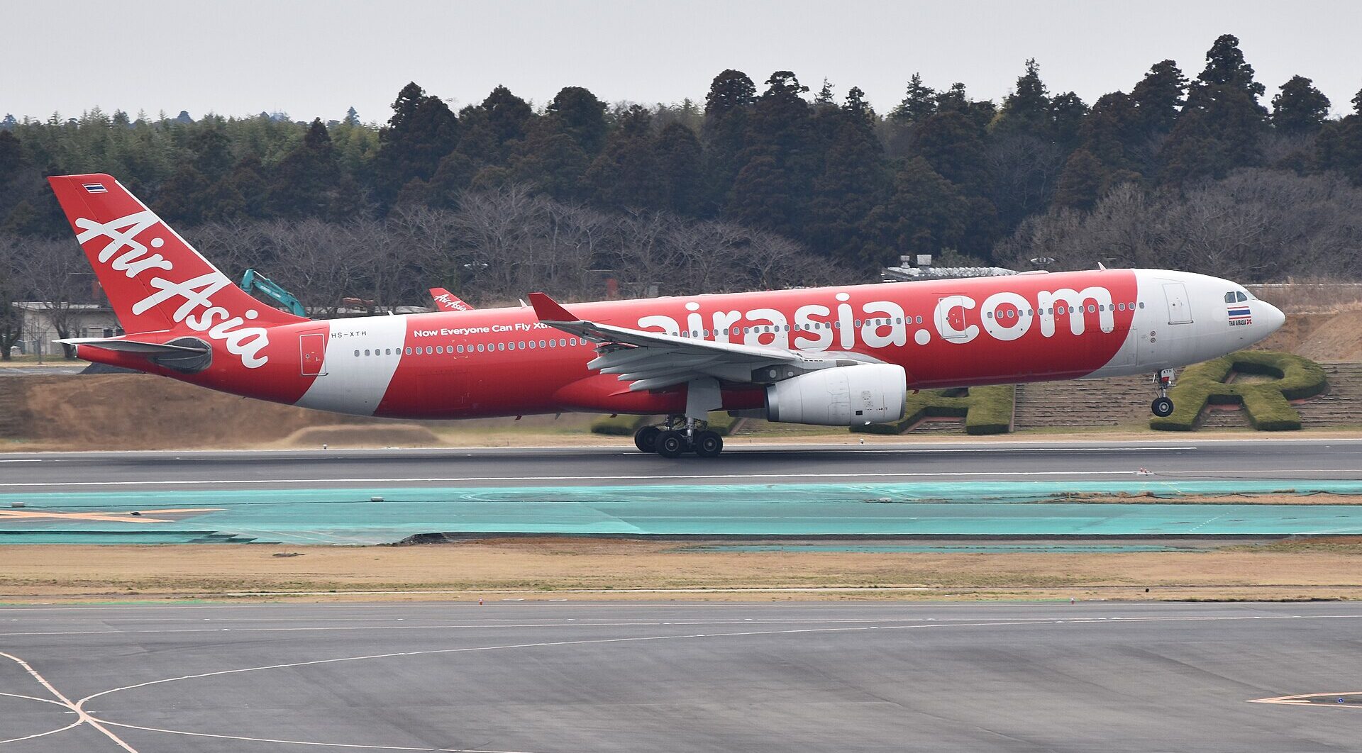 Airbus A330-343 Air Asia aircraft about to take off from the runway. Grey sky and trees in the background. White and red livery.
