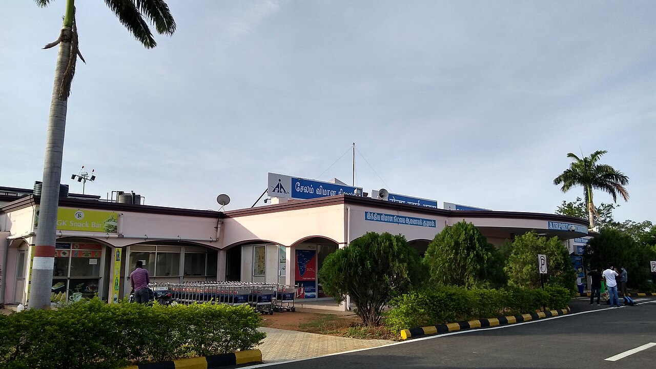 The facade of Salem Airport in India showing the terminal area in a daylight with luggage trolley placed at the terminal front with a small eatery in the building