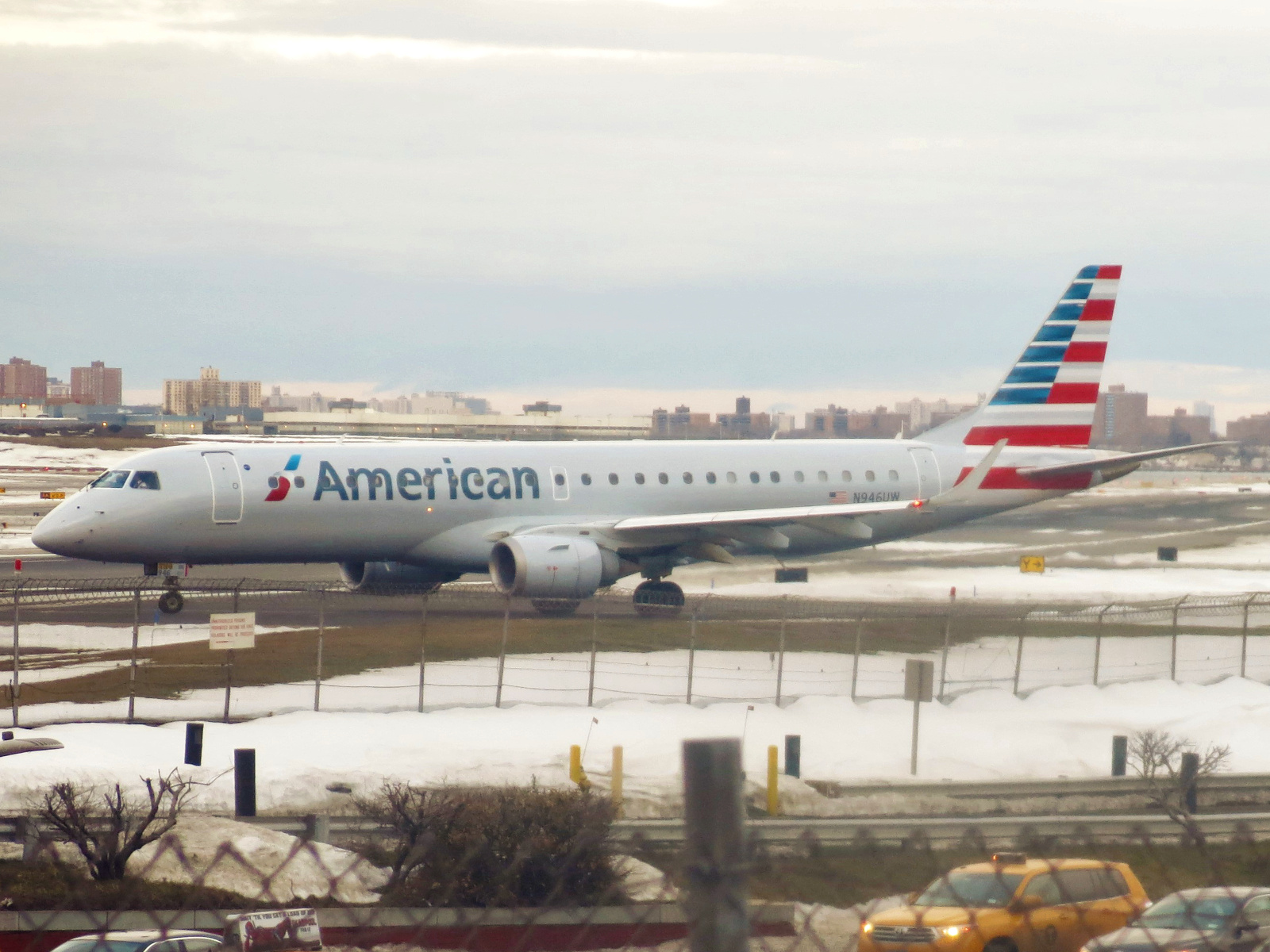 An American Airlines Embraer E-Jet is taxiing into the takeoff position at LaGuardia Airport. The aircraft occupies the entire centre of the image, with the nose positioned at the centre left of the image. 