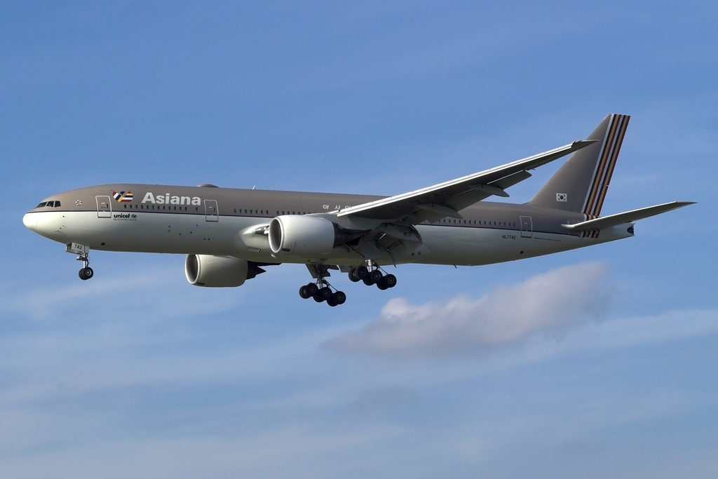 Asiana Airlines Boeing 777 flying under a blue sky. Grey and white livery.