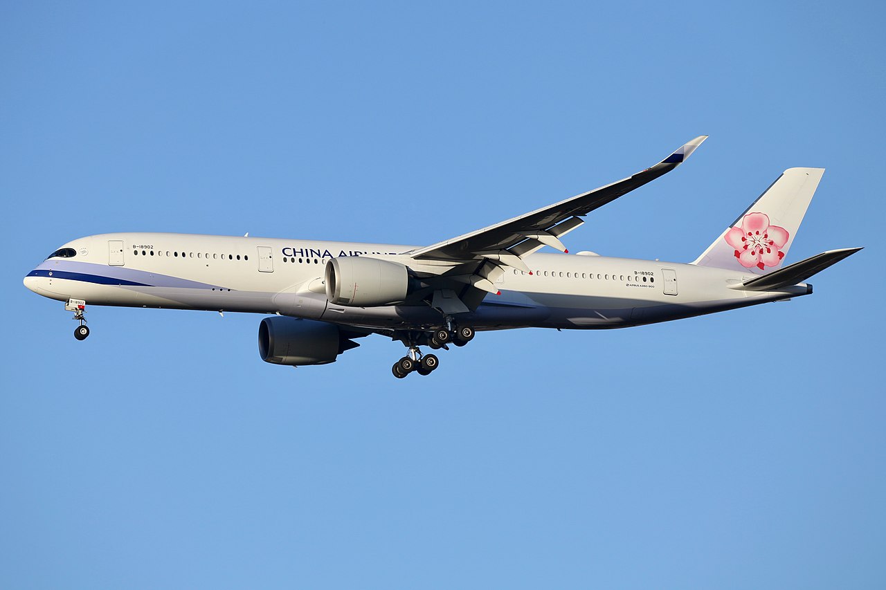 China Airlines aircraft flying amid blue skies. The aircraft has a pink flower on the back of it and wheels ready for landing. 