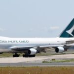 Cathay Pacific Cargo aircraft on a runway, amid grey skies and patches of grass.