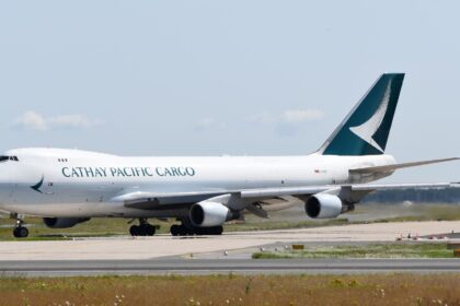 Cathay Pacific Cargo aircraft on a runway, amid grey skies and patches of grass.