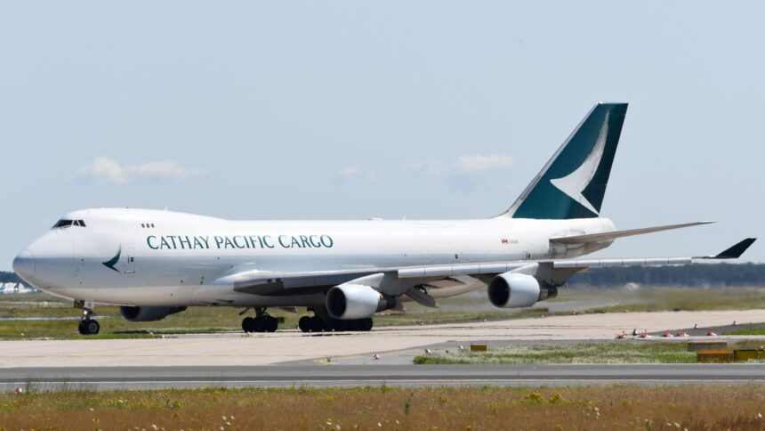 Cathay Pacific Cargo aircraft on a runway, amid grey skies and patches of grass.